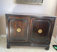 Black distressed Asian style console cabinet with decorative paneled doors and brass hardware.