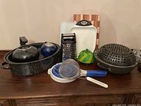 Photo showing assortment of cookware and kitchen tools including roaster pan, tea pots, steamer wok, box grater, strainers, cutting boards, and pot holder
