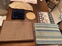 Photo showing assorted placemats and napkins including blue striped, beige woven, round coaster, snowman pattern, and blue napkin set.