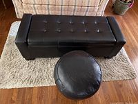 Top view of the large black leather bench with tufted surface alongside the small round black leather ottoman on a light-colored rug.