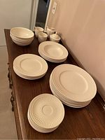 Overall view of stacked dinnerware set showing multiple plates, bowls, and mugs on wooden surface.