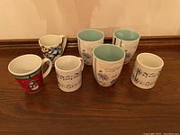 Photo showing seven ceramic mugs with various patterns including holiday, floral, and musical notes.