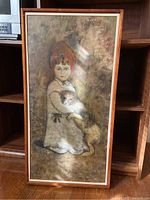 Photo of the framed painting showing a girl with red hair holding a dog, with a wooden shelf background.