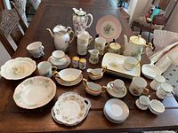 Full assortment of tea set pieces displayed on wooden table showing cups, saucers, plates, teapots, creamers, sugar bowls, salt and pepper shakers with pastel colors and floral patterns