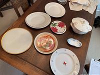 Overall view of 8 pieces including ceramic tureen with lid and assorted plates on wooden dining table.