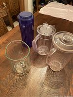Photo of four water pitchers placed on wooden table showing different materials and lid types.