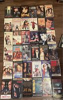 36 miscellaneous VHS movies in their original cases spread on a flat surface, showing front covers, which include well-known titles spanning various genres.