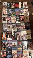 Photo showing a selection of 30 VHS movies spread on the floor, mostly the front covers with titles like Dr. Dolittle, Vampire's Kiss, The Cutting Edge, Cats Eye, Overboard and more.
