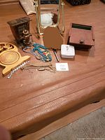 Photo showing the overall lot on a brown leather surface: antique Pana-vue mirror, wooden circular carved box, wooden decorative box, porcelain jewelry box, assorted costume jewelry.