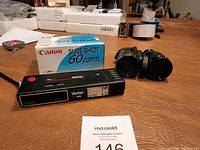 Canon Sure Shot 60 Zoom camera with original box, Vivitar Tole camera, and black binoculars on a table.