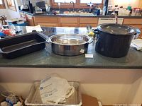 Overview of the large blue speckled canner pot with black lid, rectangular black roasting pan, and round stainless steel roasting pan on kitchen counter.