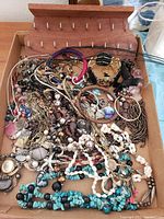 Photo showing an open box with assorted costume jewelry including necklaces, bracelets, and pendants in various colors and materials