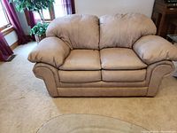 Front view of beige synthetic leather loveseat with plush armrests and cushions on a light carpet