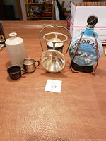 Lot displayed showing all items including vase, clock, two metal cups, and lantern on a wooden table