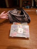 Gray fabric duffle bag and two clear plastic containers filled with embroidery and beading supplies on a wooden table.