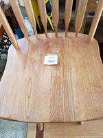 Close-up of the wooden seat surface showing natural wood grain and a numbered tag on the stool.