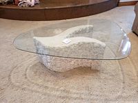 Angled view of coffee table showing curved stone base and freeform glass top