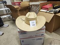 Beige Bailey Straus cowboy hat on top of a USPS Priority Mail box in cluttered room