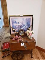 Wide shot of framed watercolor, mantel clock, vase, wall sconces and decor on wooden chest