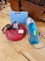 Roomba robot vacuum round red unit with charging base and power adapter with Dirt Devil handheld carpet shampooer in white and blue.