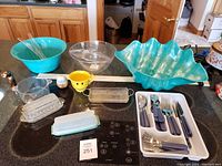 Kitchen counter with plastic bowls, glass butter dish, and silverware set.