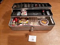 Metal tackle box open displaying organized fly fishing gear inside various trays