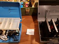 Three plastic tackle boxes open with contents visible, including fishing reels and lure trays