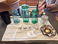 Overview of lot on cloth: three green Ball jars, black vase, four small ceramic birds, glass canister with clasp, decorative dish.