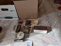 Photo showing Lutrix adapter box, shaving kit, metal bank, old clock and small items laid out on a cloth surface.