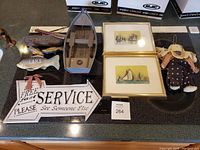 Photo showing the decorative wooden boat, wooden Welcome Lake sign with fish shapes and paddle, two framed boat pictures, cloth doll in star-patterned outfit