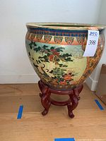 Full view of ceramic planter decorated with crane and nature motifs on wooden stand, showing colorful exterior and shape.