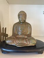 Front view of brass seated Buddha on black plastic stand