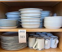 Various stacked plates and mugs, showing white ceramic items with Dansk Bistro pattern and solid white pieces.