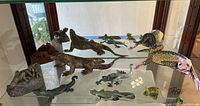 Glass display cabinet with multiple decorative lizards on three shelves including wood, metal, plastic pieces