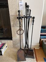 Full view of the fireplace tool set with four tools and stand shown upright on stone hearth.