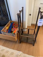 Overall view of iron log holder with fireplace tools and cardboard box with fire starters and lighters inside.