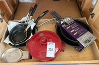 Drawer containing red Emile Henry ceramic covered pot, flatware resting plate, multiple pans including stainless steel and non-stick, and two Anolon French skillets in packaging.