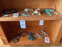 Shelf displays 12 gecko and lizard themed decorative items including metal wall hangings, ceramic candle holder, and tiles.