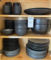 Twelve matte black bowls and two larger salad bowls on middle shelf
