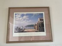 Framed limited edition lithograph 'Owl's Head' by John Stobart featuring a coastal dock scene, signed below the image, with beige matting and wooden frame.
