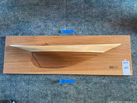 Top down photo showing the wooden half hull ship model mounted on a rectangular wooden board with two wall hanging hooks on the back.