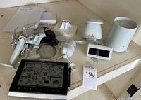 Full lot showing weather center main console, multiple sensor components including anemometer, rain gauge, UV sensor, mounting brackets, power adapter, and manual on a shelf.