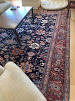 Overall view of rug laid out under furniture showing cobalt blue field and red border