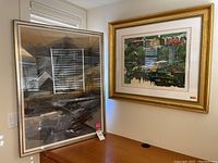 Two framed artworks side by side on a desk with window reflection