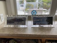 Pair of elongated rectangular picture frames made of clear crystal with vertical ridge pattern along the edges placed on a countertop.