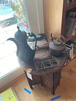 Full view of the pierced wooden circular table with metal pitcher, kettle, brass bell set and blue crab on driftwood base placed on and around the table.