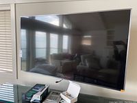Front view of Samsung 65" TV mounted on wall with remotes and boxes on table