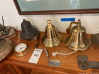 Three ship bells on shelf including dark bronze bell, stepped brass bell, polished brass bell with pull cord