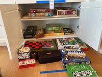 Wide-angle photo of a cabinet shelf and floor showing many boxed and unboxed games and puzzles, including chess sets, poker chips, Sorry!, and others.