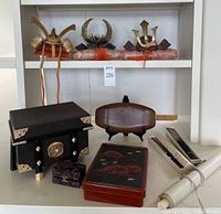 Front view showing samurai helmet ornaments on pillows atop shelving, stress ball box, lacquer storage box, wooden tray, fans and bento box